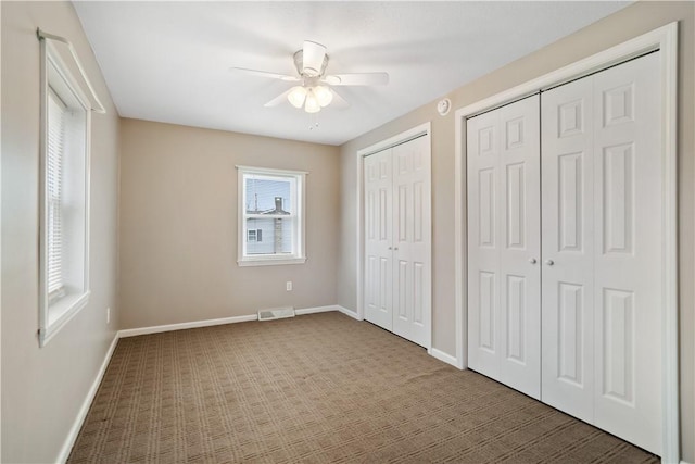 unfurnished bedroom with carpet, two closets, and ceiling fan