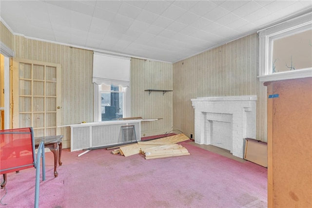 carpeted living room featuring radiator heating unit, crown molding, and a brick fireplace