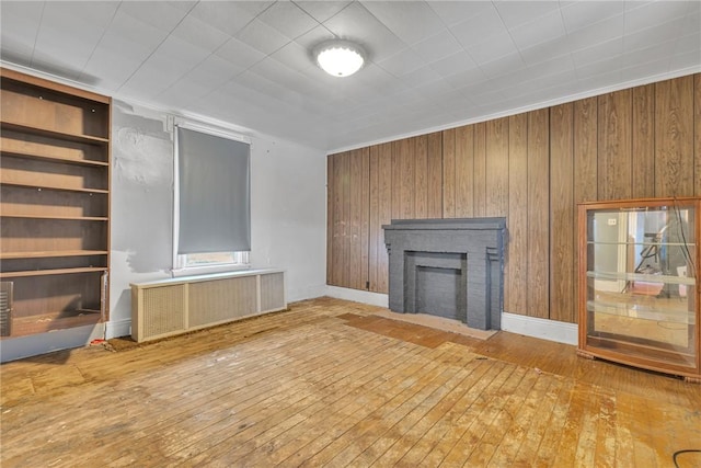 unfurnished living room with a fireplace, radiator heating unit, built in features, and wood-type flooring