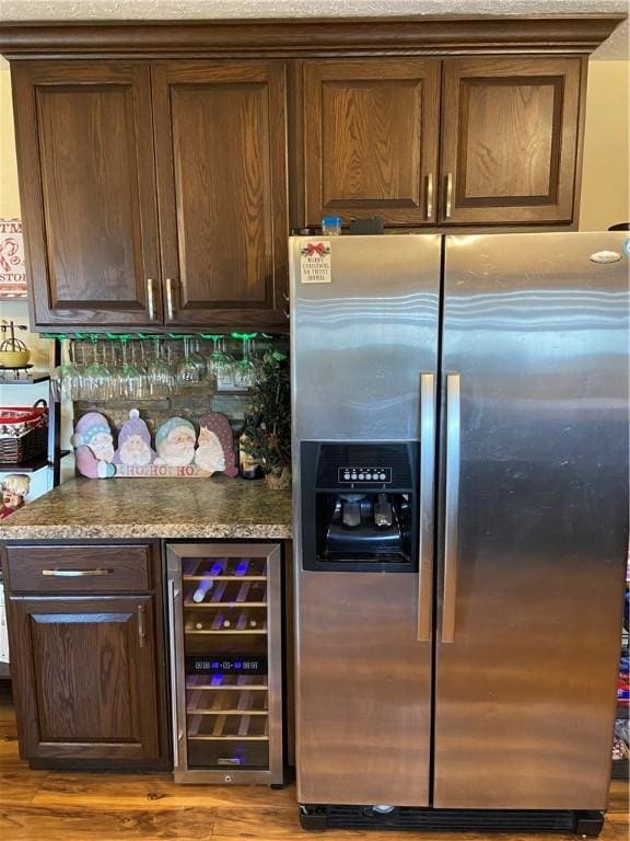 kitchen with stainless steel refrigerator with ice dispenser, dark stone counters, dark brown cabinetry, light hardwood / wood-style flooring, and wine cooler