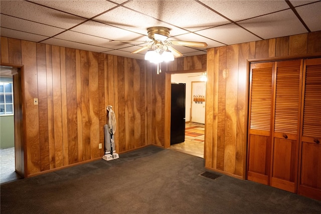 unfurnished bedroom with ceiling fan, a closet, dark carpet, and wooden walls