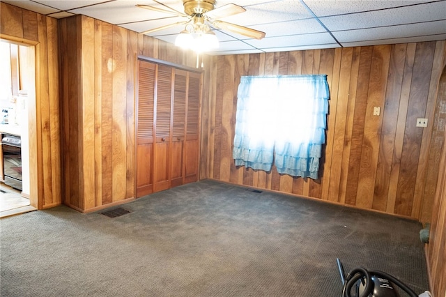 empty room featuring carpet, a paneled ceiling, ceiling fan, and wooden walls