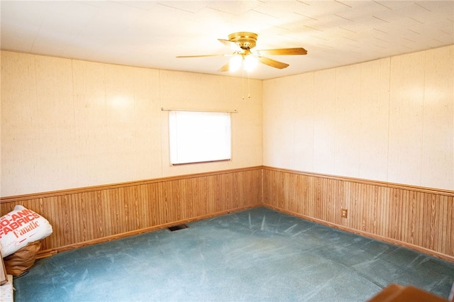 spare room with dark carpet, ceiling fan, and wooden walls