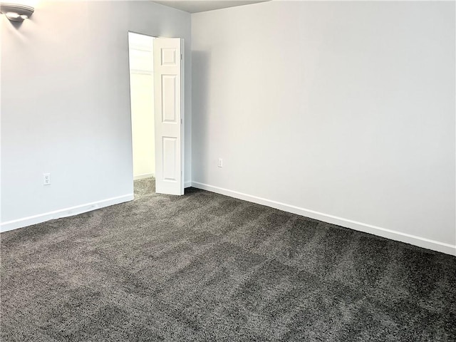 unfurnished room with baseboards and dark colored carpet