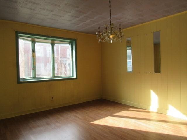 empty room with a chandelier, wooden walls, and wood-type flooring