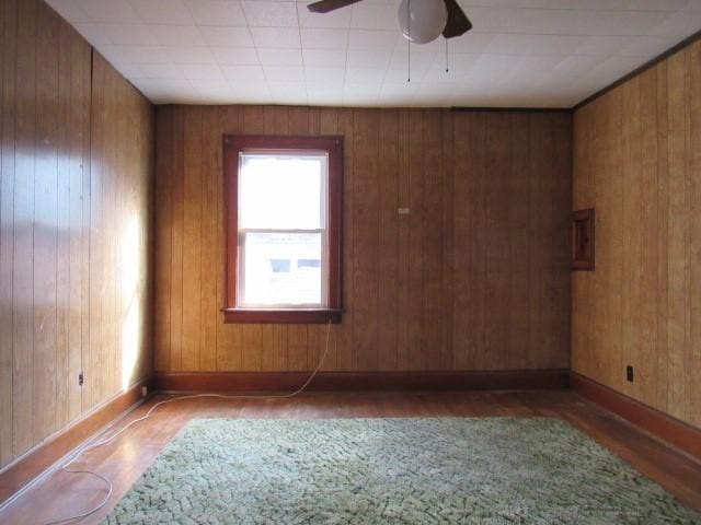 unfurnished room featuring hardwood / wood-style flooring, ceiling fan, and wood walls