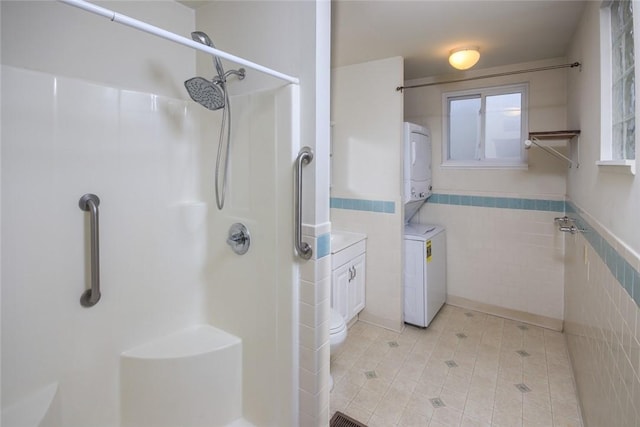 bathroom with tile walls, vanity, stacked washer / drying machine, tile patterned floors, and walk in shower