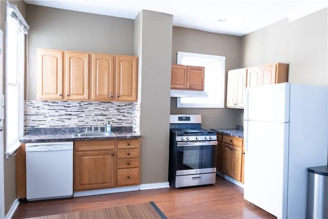 kitchen with sink, dark stone countertops, dark hardwood / wood-style flooring, white appliances, and decorative backsplash