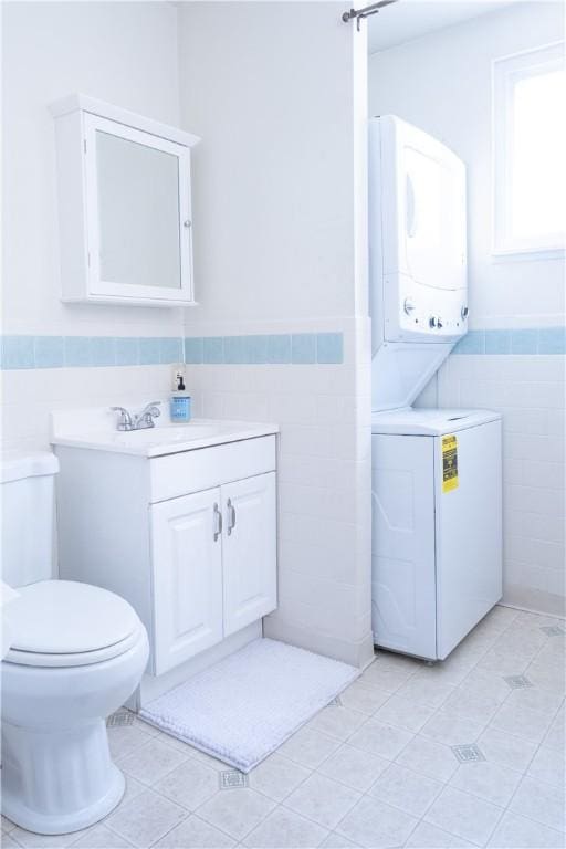 laundry area with stacked washing maching and dryer, sink, tile walls, and light tile patterned floors