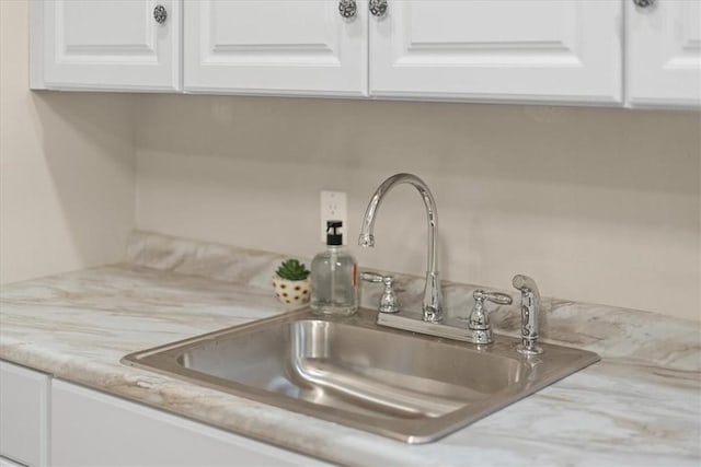 room details with light stone counters, white cabinetry, and sink