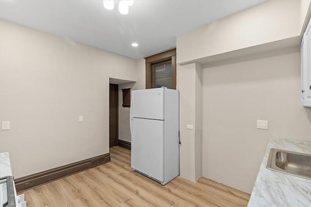 kitchen with white fridge, light wood-type flooring, sink, and white cabinetry