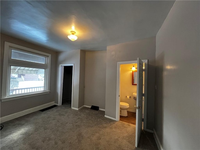 unfurnished bedroom featuring ensuite bathroom, a closet, and dark colored carpet