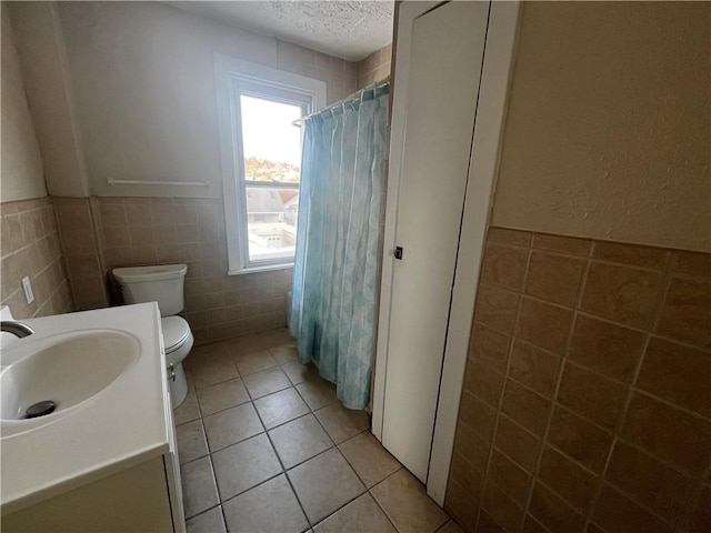 bathroom with vanity, a textured ceiling, tile walls, tile patterned flooring, and toilet