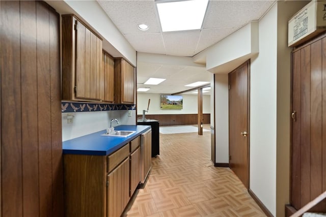 kitchen with a paneled ceiling, light parquet floors, wood walls, and sink