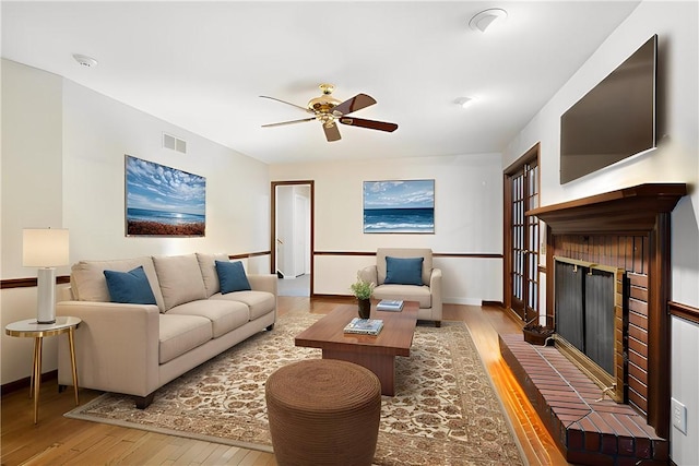 living room with hardwood / wood-style flooring, ceiling fan, and a brick fireplace