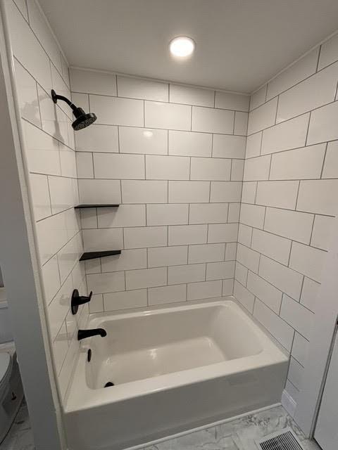 bathroom featuring tiled shower / bath combo and toilet