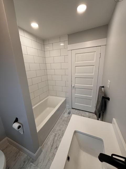 bathroom with toilet and tiled shower / bath