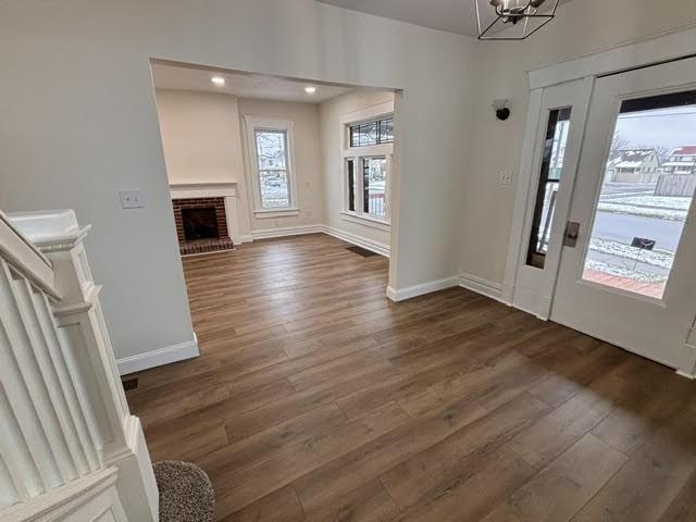 entrance foyer with an inviting chandelier, dark hardwood / wood-style flooring, and a brick fireplace