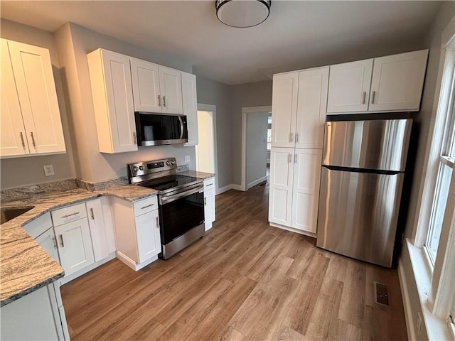 kitchen featuring sink, light stone countertops, appliances with stainless steel finishes, light hardwood / wood-style floors, and white cabinetry