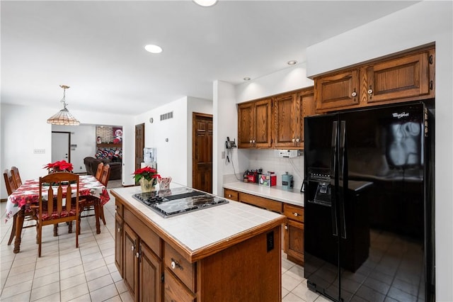 kitchen featuring a center island, black refrigerator with ice dispenser, hanging light fixtures, tile counters, and stainless steel gas cooktop