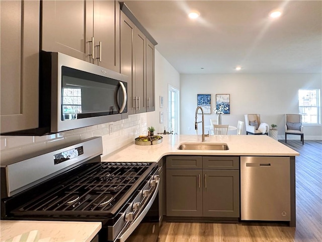 kitchen with sink, stainless steel appliances, light hardwood / wood-style flooring, kitchen peninsula, and decorative backsplash