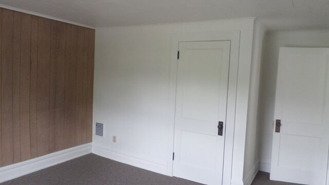 unfurnished bedroom with dark colored carpet, ornamental molding, and wood walls