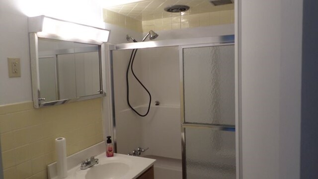 bathroom with shower / bath combination with glass door, vanity, and tile walls