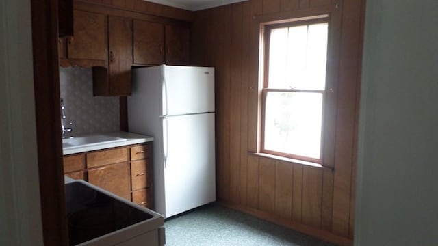 kitchen featuring white fridge, range, sink, and wooden walls