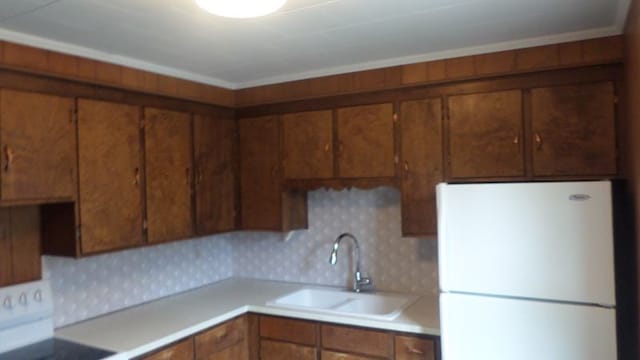 kitchen featuring stove, backsplash, white refrigerator, sink, and ornamental molding