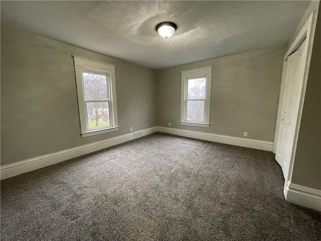 unfurnished bedroom with a textured ceiling, dark carpet, and multiple windows