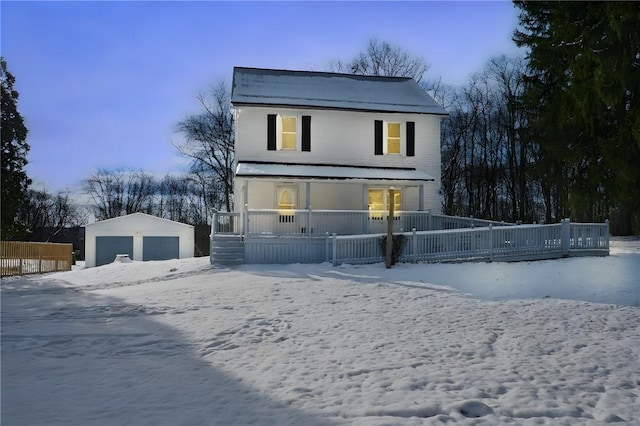 snow covered rear of property with covered porch, an outdoor structure, and a garage