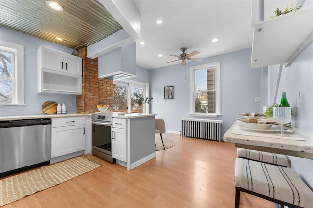 kitchen featuring radiator, white cabinets, custom exhaust hood, and appliances with stainless steel finishes