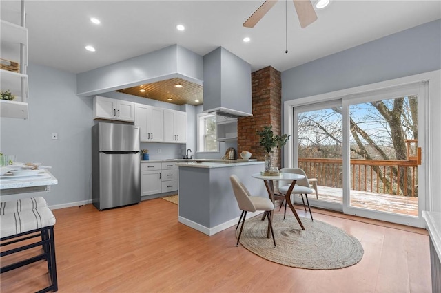 kitchen featuring stainless steel fridge, light wood-type flooring, range hood, white cabinetry, and a breakfast bar area