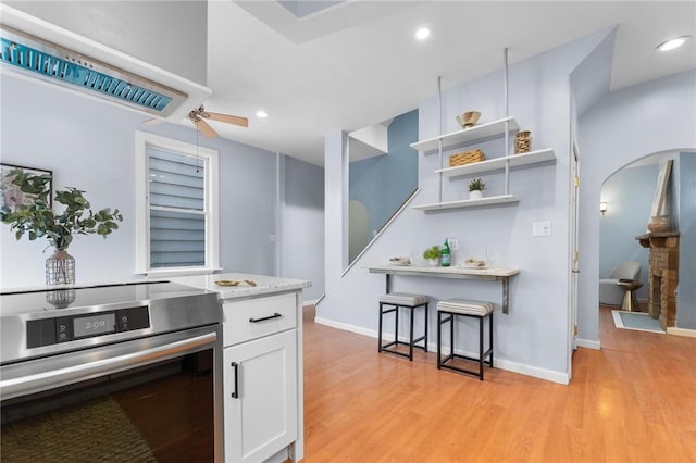 kitchen featuring ceiling fan, stove, white cabinetry, and light hardwood / wood-style flooring