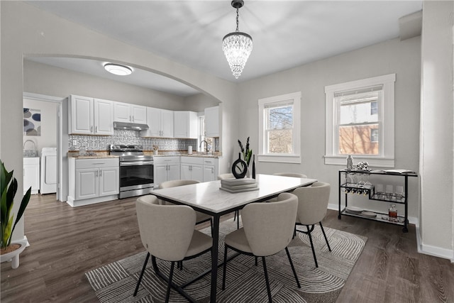 dining area featuring a notable chandelier, washer and dryer, sink, and dark wood-type flooring