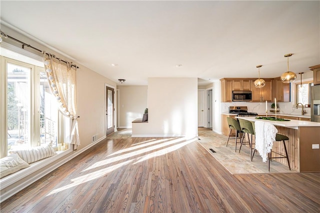 kitchen featuring a kitchen bar, light wood-type flooring, stainless steel appliances, sink, and pendant lighting