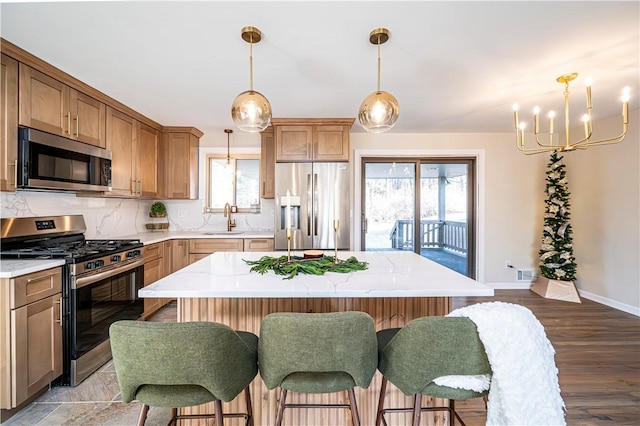 kitchen with decorative backsplash, appliances with stainless steel finishes, sink, a kitchen island, and hanging light fixtures