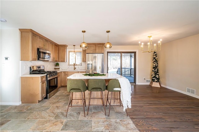 kitchen featuring appliances with stainless steel finishes, a breakfast bar, pendant lighting, a notable chandelier, and a kitchen island