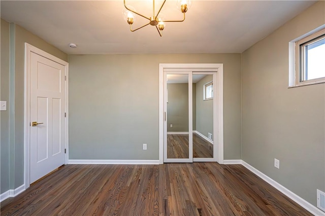 unfurnished room with a chandelier and dark wood-type flooring