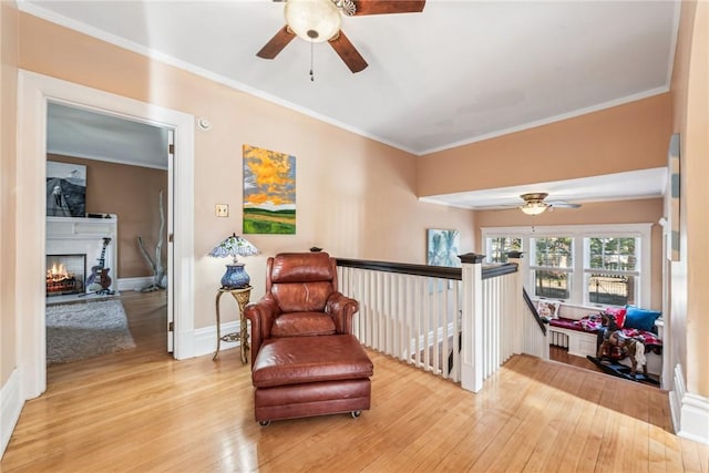 living area with a brick fireplace, ceiling fan, ornamental molding, and light hardwood / wood-style flooring