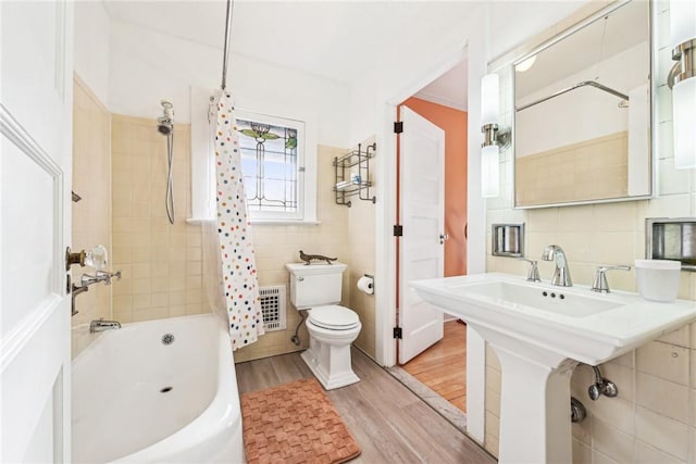 bathroom with hardwood / wood-style floors, toilet, tile walls, shower / tub combo with curtain, and heating unit