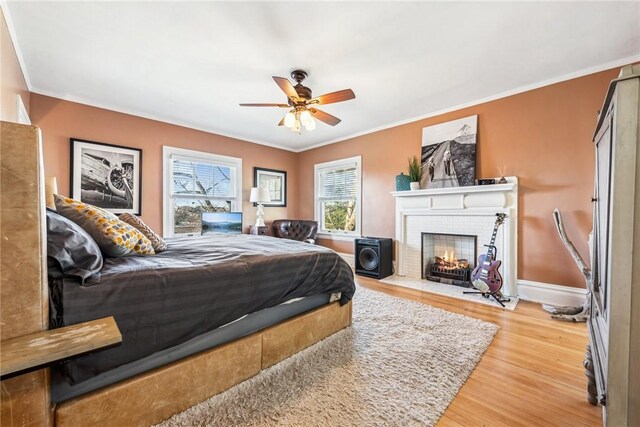 bedroom featuring ceiling fan, crown molding, wood-type flooring, and a fireplace