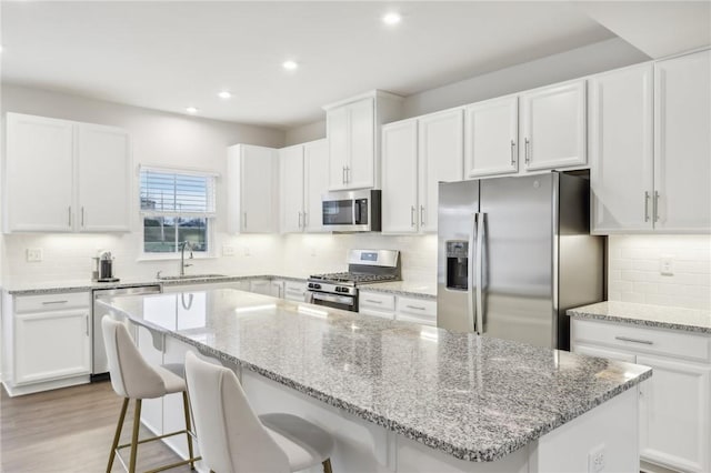 kitchen with sink, a kitchen island, a breakfast bar area, white cabinets, and appliances with stainless steel finishes