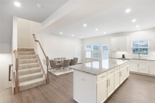 kitchen featuring a center island, sink, white cabinetry, light stone counters, and wood-type flooring