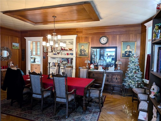 dining area featuring wood walls, a raised ceiling, parquet flooring, and an inviting chandelier