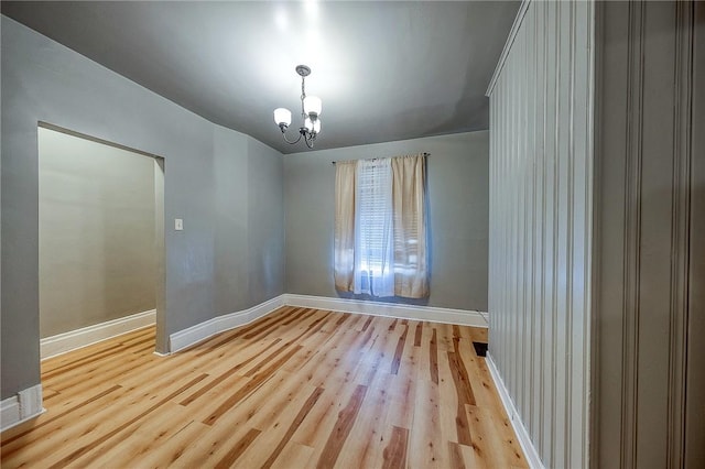 empty room featuring a notable chandelier and light wood-type flooring