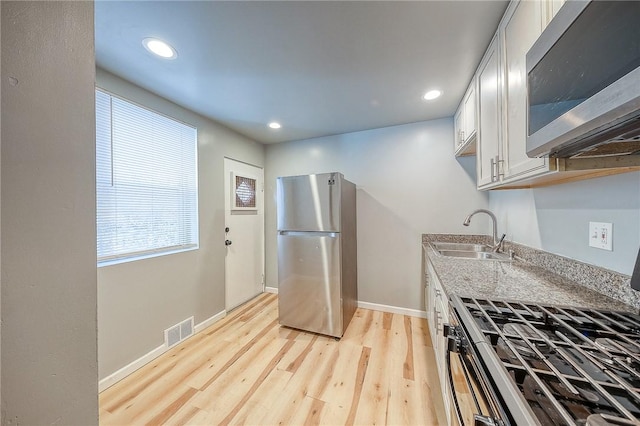 kitchen with sink, white cabinets, stainless steel appliances, and light hardwood / wood-style floors