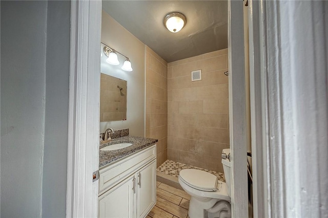 bathroom featuring a tile shower, vanity, and toilet