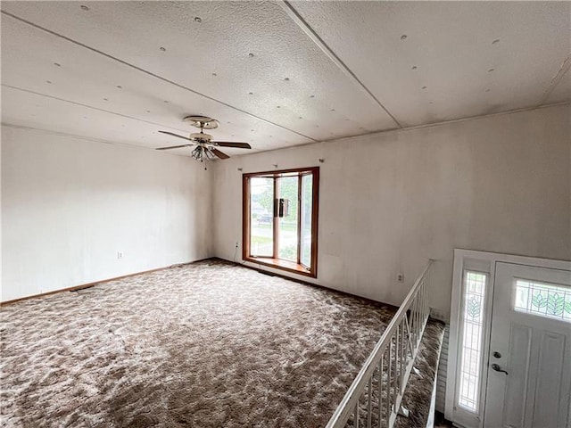 entryway with ceiling fan, plenty of natural light, carpet, and a textured ceiling