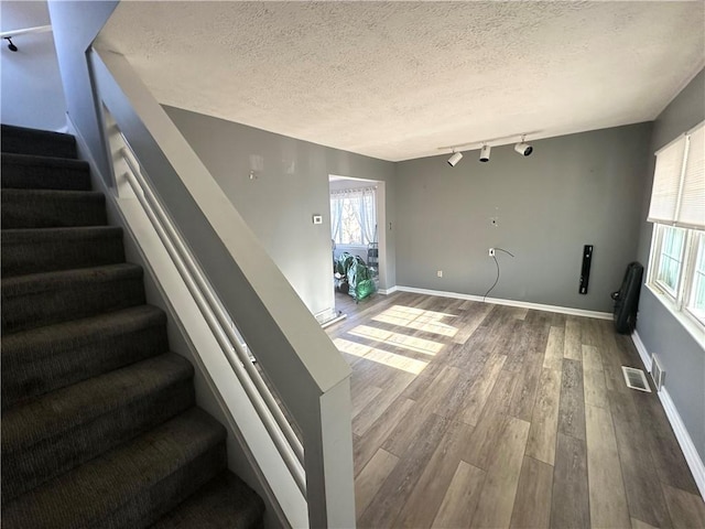 interior space featuring a textured ceiling, rail lighting, and hardwood / wood-style floors